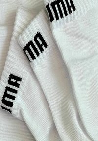 Drei Paar weiße Baumwollsocken mit gerippten Bündchen. Schwarzes Markenlogo, das nahe der Oberseite eingestrickt ist. Glatte Textur und einfaches Design.