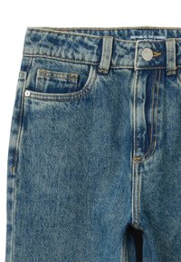 Jeans de mezclilla azul con un acabado ligeramente descolorido. Cuentan con un diseño clásico de cinco bolsillos, costuras doradas y un cierre de botón de metal.