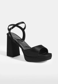Schwarze hochhackige Plateausandalen mit satinierter Oberfläche, quadratischem Blockabsatz, offener Zehenpartie und überkreuzten Knöchelriemen für einen sicheren Halt.