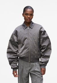 Giacca bomber grigia con maniche oversize, dettagli metallici e motivo logo ricamato. Presenta una chiusura con zip e un design del colletto.