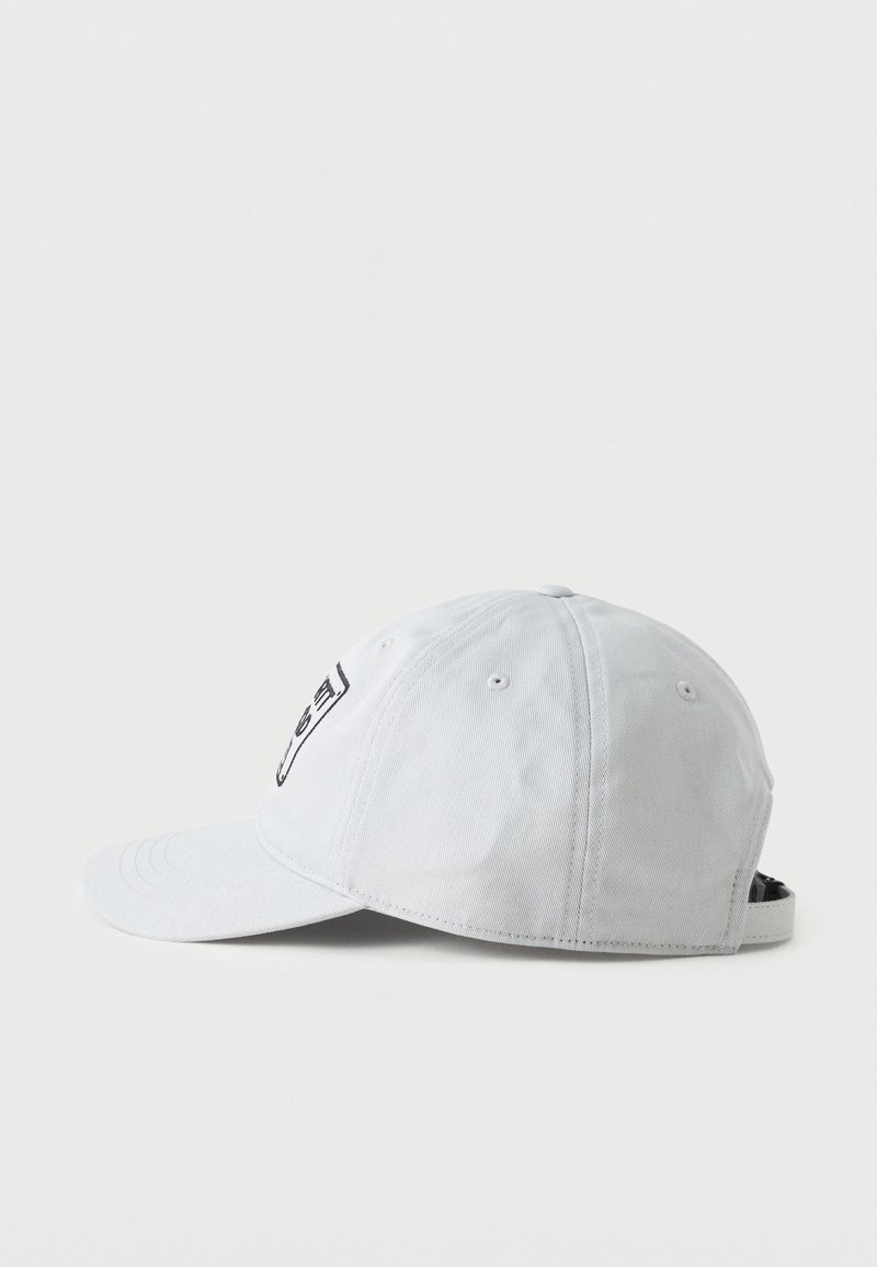 Gorra de béisbol gris claro con seis paneles, ojales de ventilación, visera curva y correa ajustable, mostrada desde el lado izquierdo sobre fondo blanco.