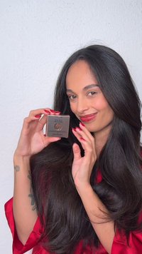 Kvinne med langt mørkt hår og røde negler holder Lancôme Idôle Sparkling Comet øyenskygge og smiler mot en hvit bakgrunn.