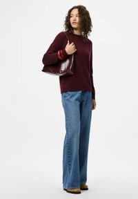 Bordo pleteni pulover, sproščen kroj. Svetlo modri zvonasti kavbojki, svetla pranje. Sijajna bordo torbica z naramnico. Rjavi gležnjarji.