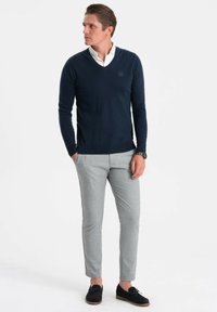 Maglione a V in navy realizzato in tessuto a maglia, abbinato a pantaloni grigi chiari su misura e scarpe in suede nere. Design semplice, silhouette aderente.