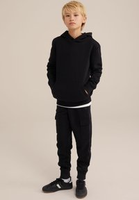 Felpa nera con cappuccio e tasca a marsupio, abbinata a pantaloni cargo neri con tasche laterali. Completato con sneakers nere.