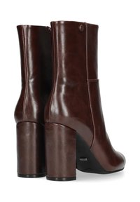 Botines de cuero marrón hasta el tobillo con un alto tacón de bloque. Textura suave, diseño elegante y cremallera lateral con un discreto detalle de logo.