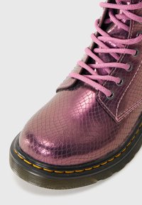 Stivale metallico rosa con un motivo a pelle di serpente testurizzato, dotato di lacci rosa e suola nera con cuciture gialle.