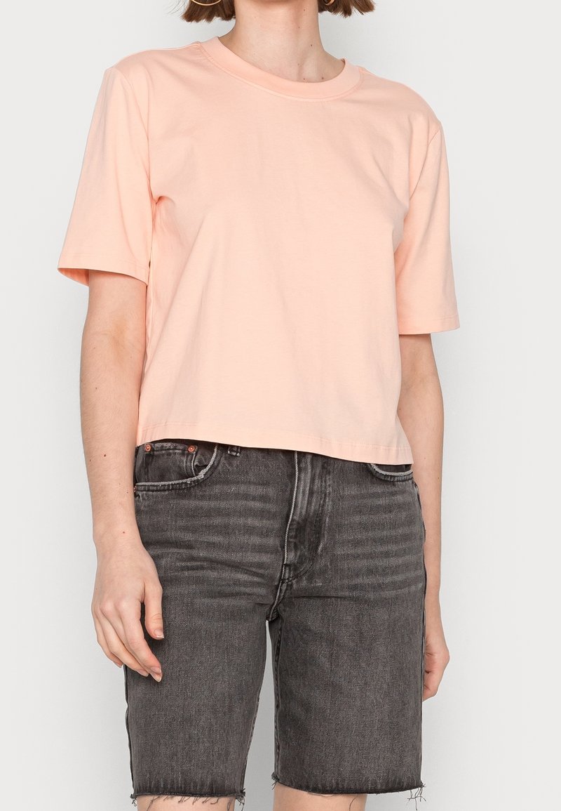 Personne portant un t-shirt à manches courtes couleur pêche clair et un short en jean noir délavé taille haute avec des ourlets effilochés.