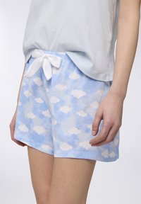 Shorts in cotone azzurro chiaro con motivi di nuvole bianche, una vita elasticizzata e un nastro bianco legato davanti.