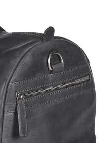 Mochila de cuero negro con forma redondeada, que cuenta con un bolsillo frontal con cremallera y un adorno de anillo en D de metal. Detalle de costura visible.