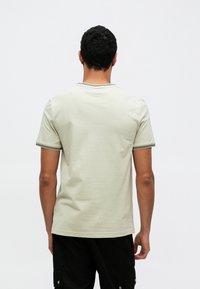 Ανοιχτοπράσινο κοντομάνικο μπλουζάκι με μαύρο ριμπ γιακά και λεπτομέρειες στα μανίκια, με λείο, απαλό ύφασμα και απλό σχέδιο.