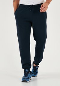 Navyblauwe joggingbroek van zacht materiaal, met een elastische tailleband met een trekkoord, zijzakken en taps toelopende pijpen.