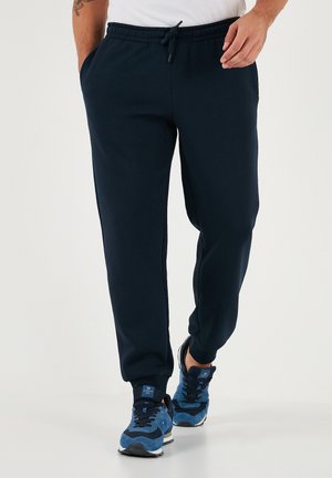 Navy blue sweatpants made of soft fabric, featuring an elastic waistband with a drawstring, side pockets, and tapered legs.