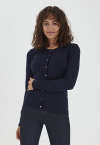 Cardigan blu navy con design aderente, maniche lunghe e chiusura con bottoni. Realizzato in materiale morbido e liscio, con semplici bottoni metallici.