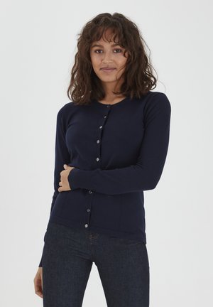 Gilet bleu marine au design ajusté, avec manches longues et fermeture à boutons. Fabriqué en matériau doux et lisse, il présente de simples boutons métalliques.