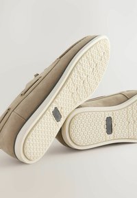 Încălțăminte din suede bej cu o talpă din cauciuc texturată. Formă rotundă, design minimalistic, având un accent subtil negru pe talpă.