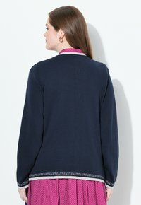 Cárdigan de punto azul marino con un escote redondo, mangas largas y acentos de dobladillo con patrones para un detalle añadido. Textura suave en general.