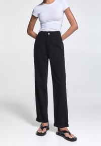 Svarta denimbyxor med vida ben, uppvikta fållar och framfickor. Kombineras med en åtsittande vit kortärmad skjorta och svarta sandaler.