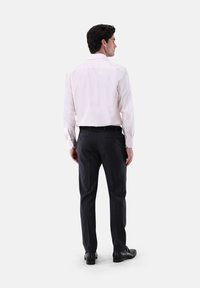 Camicia rosa chiara con maniche lunghe e colletto a punta, abbinata a pantaloni scuri e scarpe nere. Tessuto morbido, vestibilità su misura e polsini abbottonati.