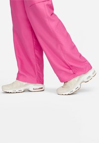 Klarröda byxor i ett mjukt material som matchas med beige Nike-sneakers med luftkuddar och texturerade detaljer.