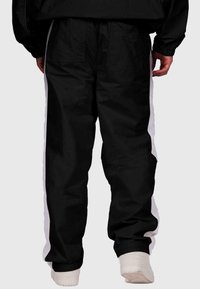 Melna kravas bikses ar baltām sānu svītrām, raksturo relaksēta fitība, divas aizmugures kabatas un elastīgas maliņas. Izgatavotas no viegla auduma.