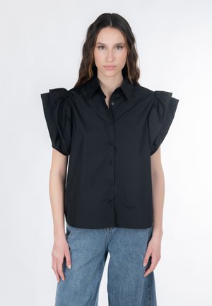 Camisa negra con mangas abullonadas, cierre con botones en la parte delantera y cuello. Combinada con vaqueros azules de pierna ancha. Textura suave, diseño minimalista.