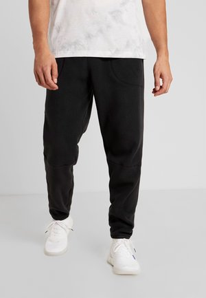 Sorte sweatpants med en afslappet pasform, der har to forlommer og teksturerede detaljer langs benene, kombineret med hvide sportssko.