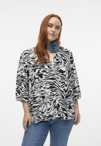 Black and white zebra print top with short sleeves and a V-neckline. Soft fabric, relaxed fit, paired with denim jeans for contrast.