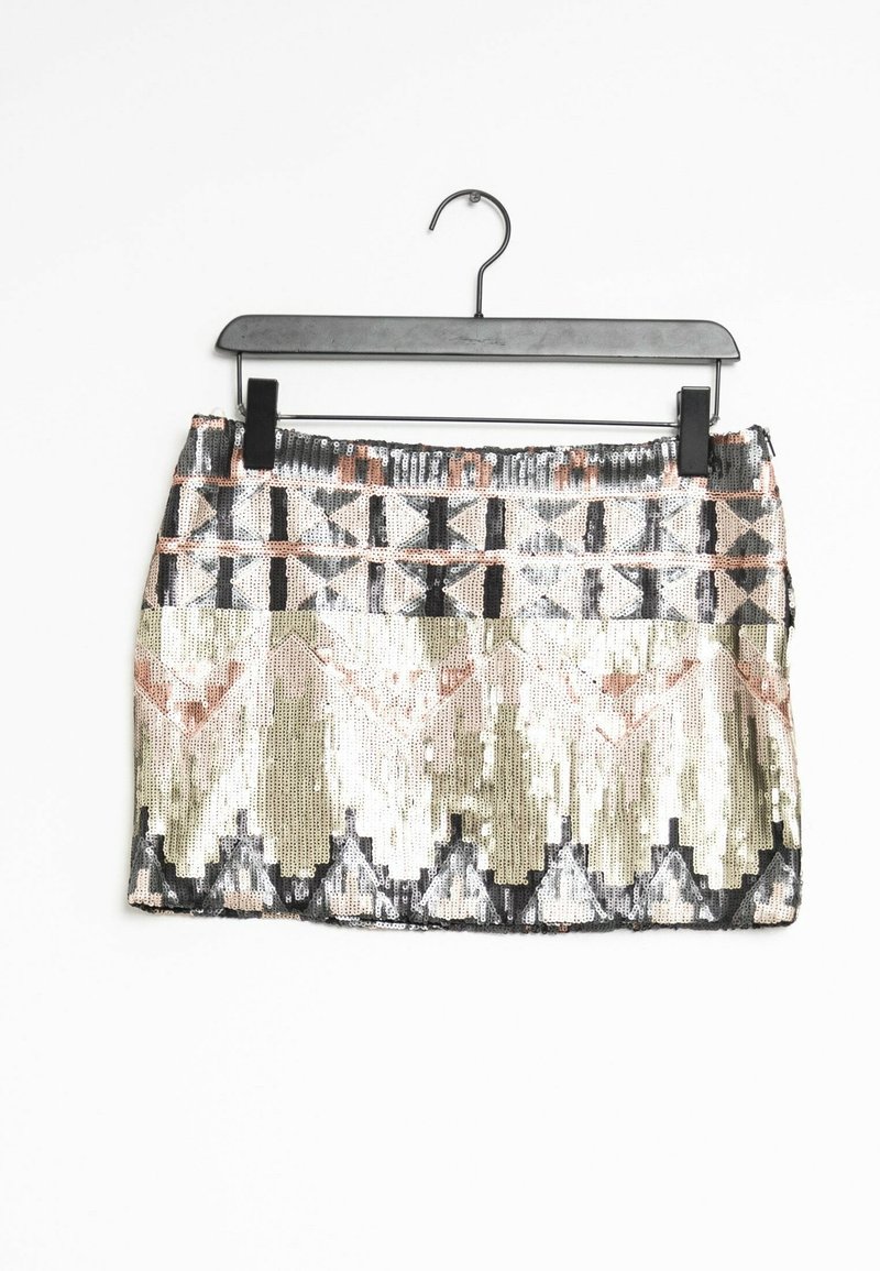 Jupe mini en sequins avec des motifs géométriques en beige métallisé, or, noir et rose. Conçue en tissu texturé, suspendue à un cintre noir.