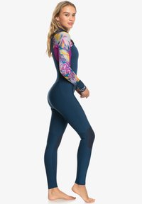 Neopreno azul marino con brazos de patrón floral, que cuenta con un cuello alto, construcción sin costuras y paneles de rodillas reforzados.