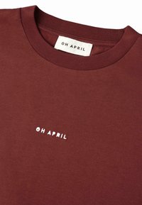 Bordo megztinis su gumuotu apykakle, priekyje su baltais siuviniais tekstu "OH APRIL". Minkšta medžiaga su lygiu paviršiumi.
