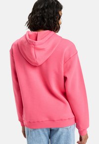 Sudadera con capucha rosa de textura suave, corte relajado y puños acanalados. La parte trasera cuenta con un estilo de bolsillo canguro clásico.