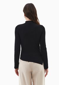 Czarna, długosleeve'owa bluzka z prążkowanego materiału, z wysokim kołnierzem, dopasowanym krój i subtelną teksturą, połączona z jasnobeżowymi, luźnymi spodniami.