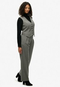 Szary kamizelka w prążki, dopasowana do spodni o wysokim stanie w tym samym kolorze, uzupełniona czarnym swetrem z długim rękawem i czarnymi botkami za kostkę.