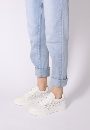 Hvide sneakers med perforeret design på siderne, flad sål, snørelukning, båret med opbrettede lyseblå cowboybukser.