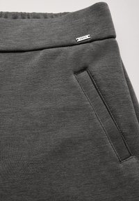 Tissu de sweat-shirt gris avec une texture lisse, présentant une taille élastique, une poche latérale et une étiquette logo en argent cousue à l'avant.