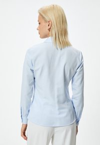 Lichtblauwe slim fit shirt met lange mouwen, een puntige kraag en knoopmanchetten. Glad textuur en subtiele glans op de stof.