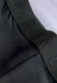 Čierna tkanina s hladkou textúrou a kontrastným elastickým pásom s reliéfnou značkou. Detailný záber zvýrazňuje materiál a šitie.