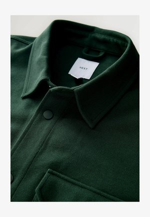 Dark green button-up shirt featuring a textured fabric, ribbed design, a pointed collar, and a chest pocket with a black button.