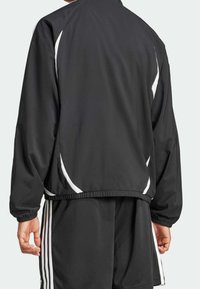 Svart trackjacka med vita detaljer, med en avslappnad passform, elastiska muddar och midja med dragsko. Gjord av mjukt, lätt material.