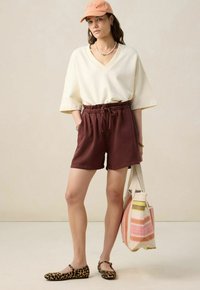 T-shirt beige clair à col en V, short marron avec taille élastique, ballerines imprimé léopard et sac fourre-tout rayé multicolore.