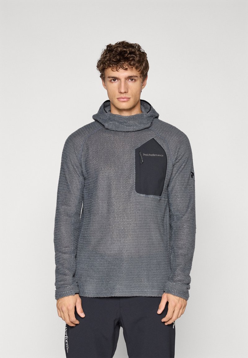 Grå teksturert langermet topp med cowl-hals og en svart brystlomme med logo. Stoffet har et vevd mønster og en avslappet passform.