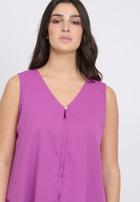 Top senza maniche di colore viola con scollatura a V, caratterizzato da un dettaglio centrale con bottone e leggero drappeggio sul seno. Tessuto morbido e leggero.