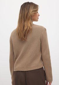 Bruine gebreide trui met een textuurafwerking, voorzien van een geweven zoomdetail. Het ontwerp heeft een relaxte pasvorm en lange mouwen.