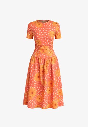 Koraalrode jurk tot op de knie met korte mouwen, getailleerde taille, witte polkadots en een groot gele bloemenpatroon over de hele stof.