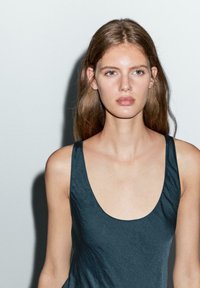 Top senza maniche di un elegante blu scuro con scollatura profonda, texture liscia e design minimalista, indossato da un modello su uno sfondo neutro.