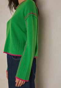 Vihreä neulepaita, jossa resorit helmassa ja hihoissa, ja reunoilla vaaleanpunaiset korostusaumat. Mukavan väljä istuvuus ja keskipitkät hihat.