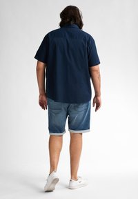 Marineblauw T-shirt met korte mouwen, denim short met omgeslagen mouwen, witte sneakers. Eenvoudig ontwerp, zachte textuur, comfortabele pasvorm en zichtbare achterkant.