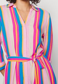 Robe rayée multicolore mettant en avant des teintes de rose, bleu et jaune, avec un col, une patte de boutonnage et une ceinture nouée à la taille.