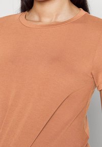 Short-sleeve, crew-neck t-shirt in a muted terracotta color, made of soft, stretchy fabric with a smooth texture and clean seams.